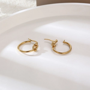 Detail shot of golden knot earrings on white ceramic tray showing sleek metal texture