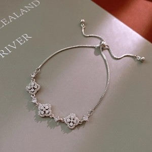 Close-up of adjustable clover charm bracelet with sparkling crystals on green background