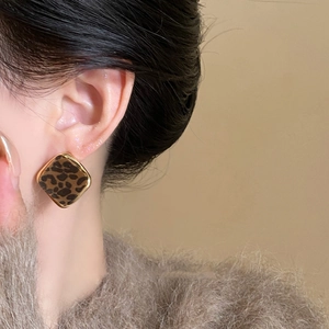 Macro shot of geometric leopard print earrings with gold trim on a female model