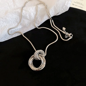 Close-up of layered silver circular pendant on snake chain over white textured paper