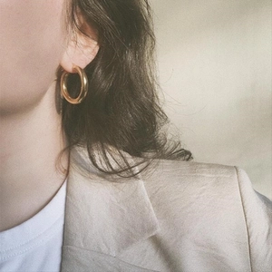 Close-up of thick gold geometric hoop earrings worn by a model in retro style