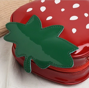 Close-up of strawberry-shaped crossbody bag with red patent leather and green leaves