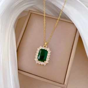 Macro shot of gold necklace with emerald square stone and zircon halo on white silk
