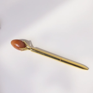 Close-up of golden metal ballpoint pen featuring an oval orange gemstone in claw setting