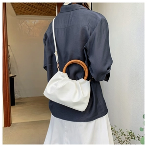Cloud crossbody bag with wooden handle and white pleated detail shown on model