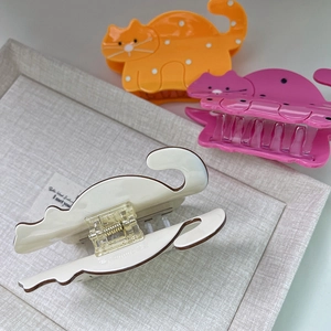 Detailed view of three cat-shaped acetate hair claws in orange, pink and cream white