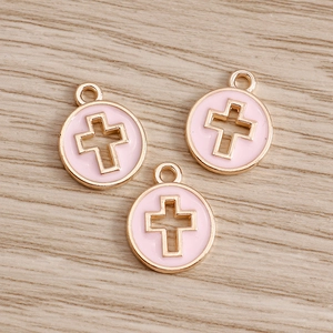 Light pink and gold hollow cross round coin pendants on a light wood background