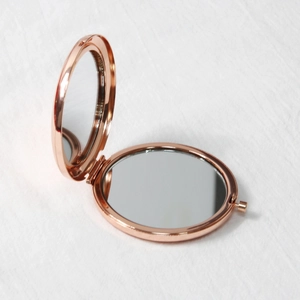 Portable rose gold round metal folding makeup mirror on white fabric background