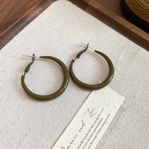 Close-up of olive green geometric round hoop earrings on a textured linen background