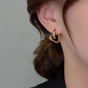 Close-up of a model wearing a minimalist gold-plated twisted heart-shaped hoop earring