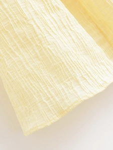 Close-up of yellow tree-pattern wrinkled fabric texture and fine stitching on the dress