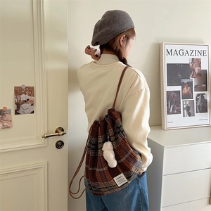 Brown plaid drawstring backpack with white plush pompom on a female model's back