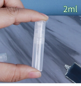Hand holding a 2ml clear plastic perfume spray bottle over marble background