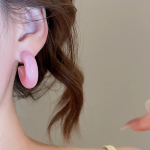 Gros plan de créoles en acrylique rose portées par un mannequin avec un éclat soyeux doux