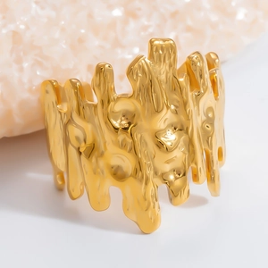 Close-up of a wide gold stainless steel ring with a unique molten texture on a pink coral