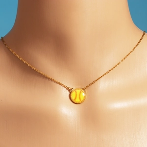 Detail showing a golden necklace with a yellow enamel softball pendant on a blue background
