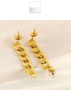 Macro detail of gold Cuban chain earrings with square zircon on light silk fabric