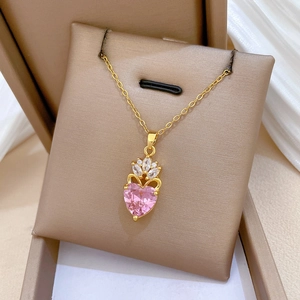 Close-up of golden crown necklace featuring a pink heart stone and sparkling crystals