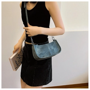 Detail of grey-blue denim texture shoulder bag with metallic buckle on a model