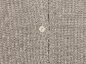 Detailed macro view of taupe knit texture and a single white button on a cardigan