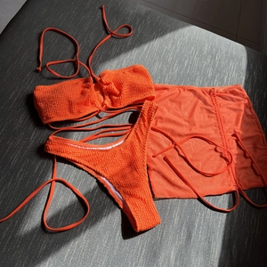 Flat lay of bright orange three-piece bikini set with ruched fabric and mesh skirt