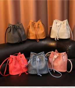 Collection of minimalist drawstring bucket bags in six neutral colors on a black leather sofa