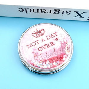 Détail d'un miroir de maquillage rond avec du sable mouvant rose et des paillettes cœur