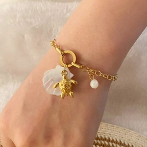 Detail of a gold turtle shell bracelet with white shell charm on a seaside holiday background