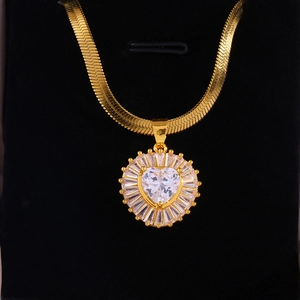 Macro detail of gold snake chain necklace with heart zircon pendant and sunburst halo