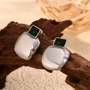 Detail of silver irregular square earrings with green zircon on natural wood surface