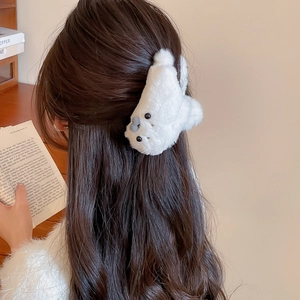 Close-up of a white plush seal hair claw clip worn on brown hair in a cozy indoor setting