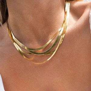 Detail van gelaagde gouden platte slangenketting op model met glanzende metaalglans