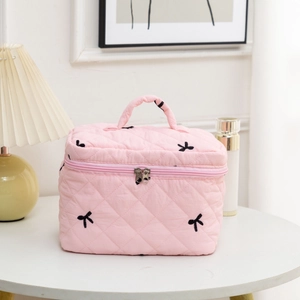 Close-up of pink quilted cosmetic bag with elegant black bow embroidery and top handle