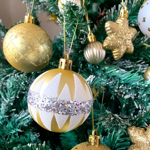 Dettaglio di ornamenti natalizi dorati e bianchi appesi su un ramo di albero di Natale