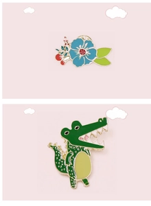 Detail of cartoon crocodile and blue flower enamel pins with gold metal edging