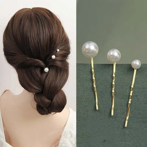 Detailed close-up of three pearl hair pins with gold metal finish on a green backdrop