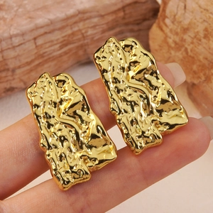 Golden irregular geometric earrings with molten lava texture shown on a hand model