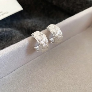 Macro shot of silver C-shaped earrings with intricate woven texture and high-polish finish