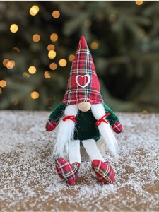 Detail of a Christmas gnome figurine with red plaid hat sitting on snowy wood surface
