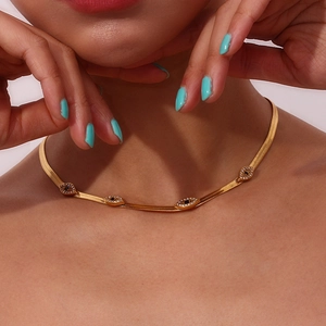 Close-up of golden flat snake chain necklace with four devil's eye charms on a model neck