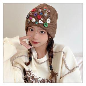 Detailed view of brown knit beanie featuring various colorful decorative buttons and textures