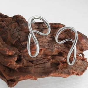 Minimalist geometric wave hoop earrings in polished silver finish on a rustic wood block
