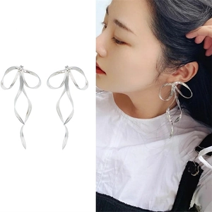 Macro shot and model wearing silver ribbon bow earrings with long metallic streamers