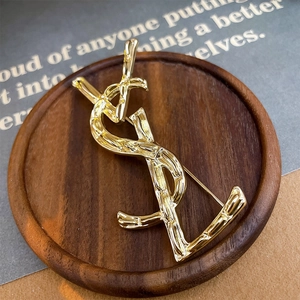 Close-up of vintage gold intertwined letter brooch with textured bamboo pattern