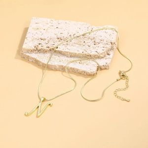 Macro detail of golden letter N pendant with zircon on a sleek snake chain necklace