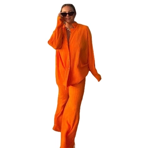 Women's pleated two-piece set featuring long sleeve orange shirt and wide-leg trousers