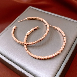 Détail de créoles en or rose ornées de pierres colorées et d'une texture perlée chic