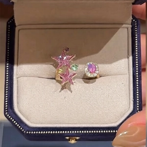 Detail of star-shaped pink stones and green gems on a gold adjustable ring in a box