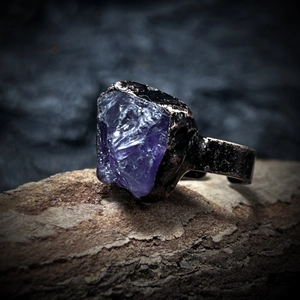 Macro shot of an unpolished purple raw gemstone on a textured dark metal ring