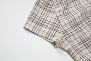 Close-up of brown plaid shirt sleeve showing fine stitching and cotton linen texture